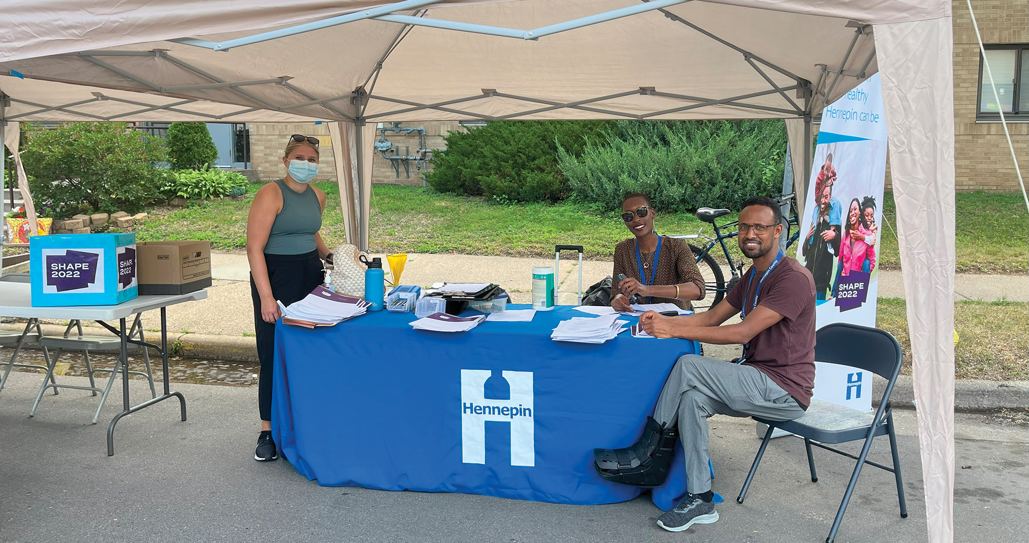 people standing beneath a tent at a table handing out surveys