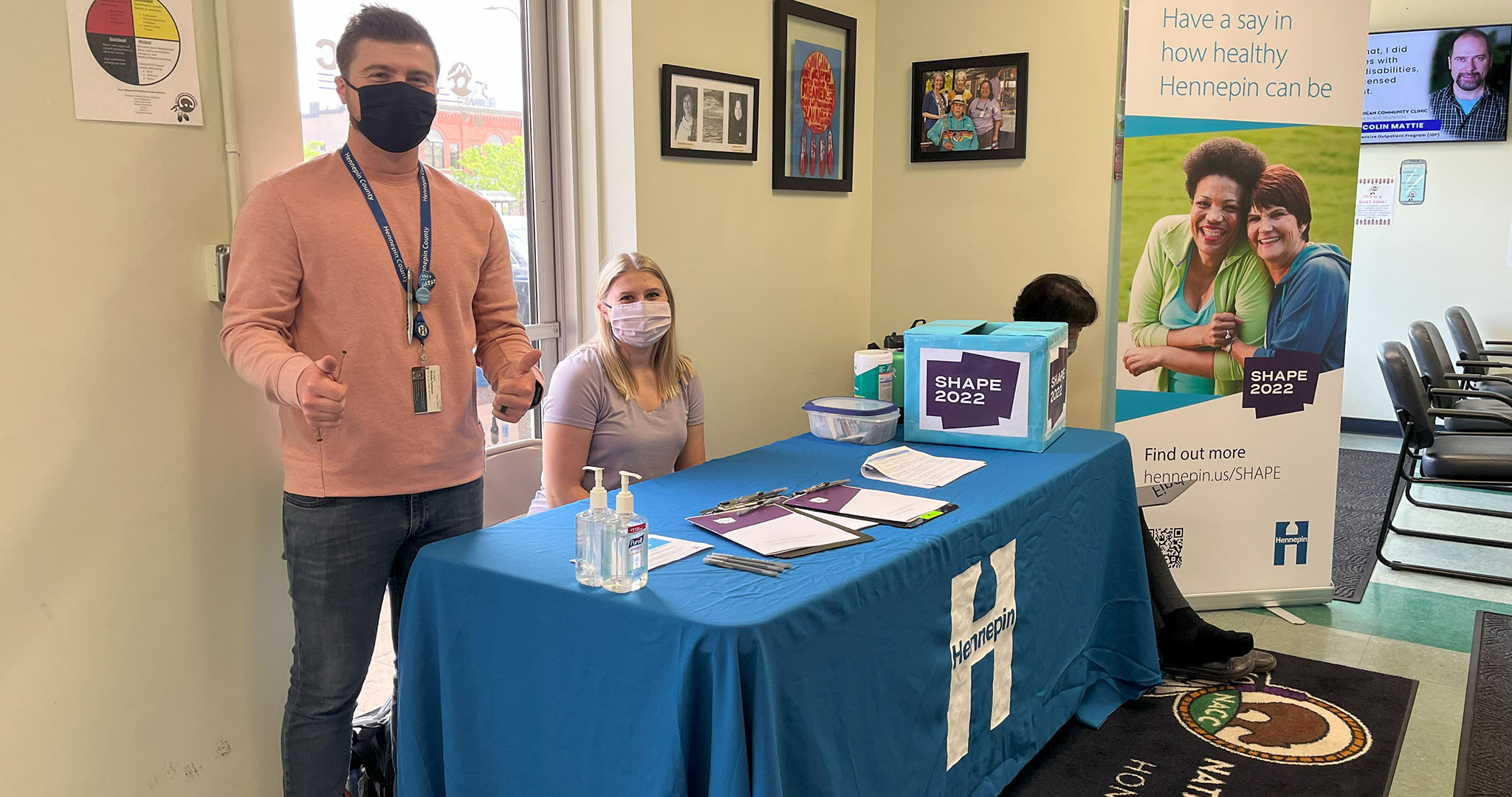 two people standing at a table wearing masks and handing out surveys