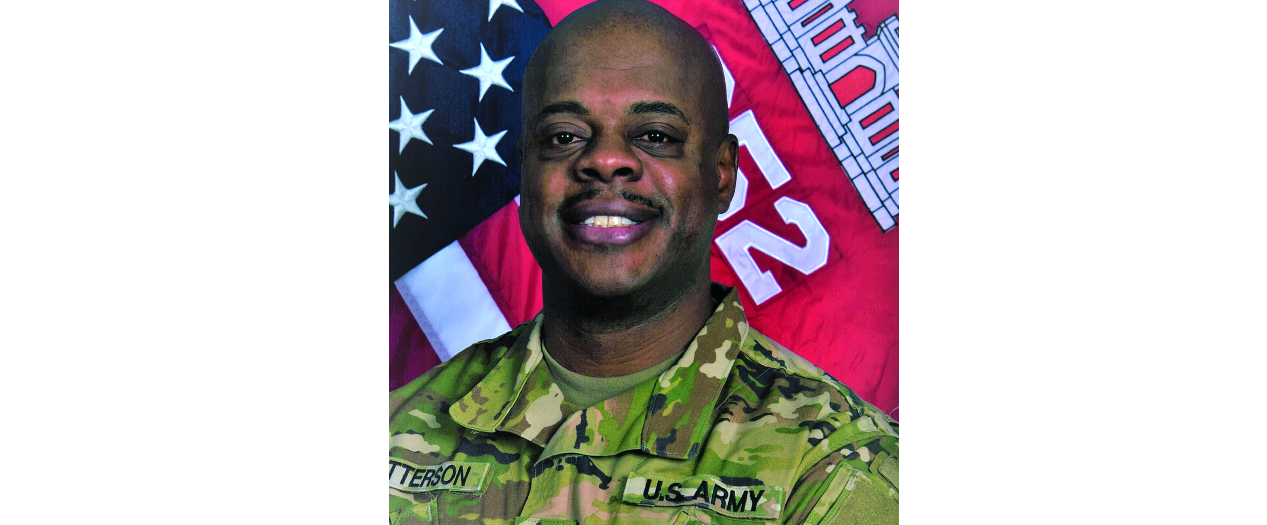 Tyrone Patterson wearing his Army uniform, in front of his unit flag and an American flag.