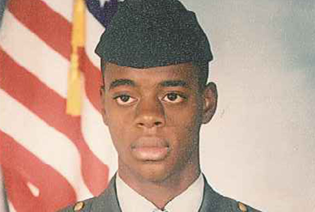 A young Tyrone Patterson wearing his Army greens, in front of an American flag.