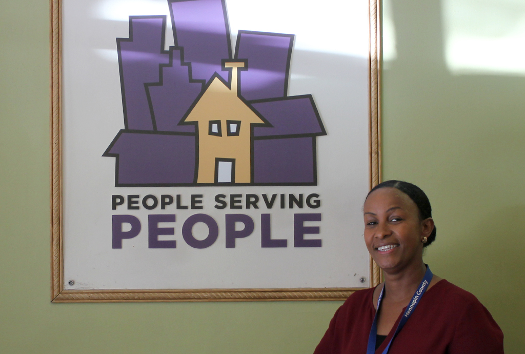 Naomy, a mental health practitioner, next to a sign for the People Serving People shelter